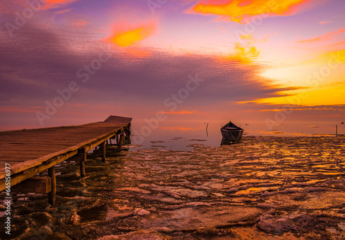 Obraz na płótnie frozen boat in winter on the lake at sunrise w salonie