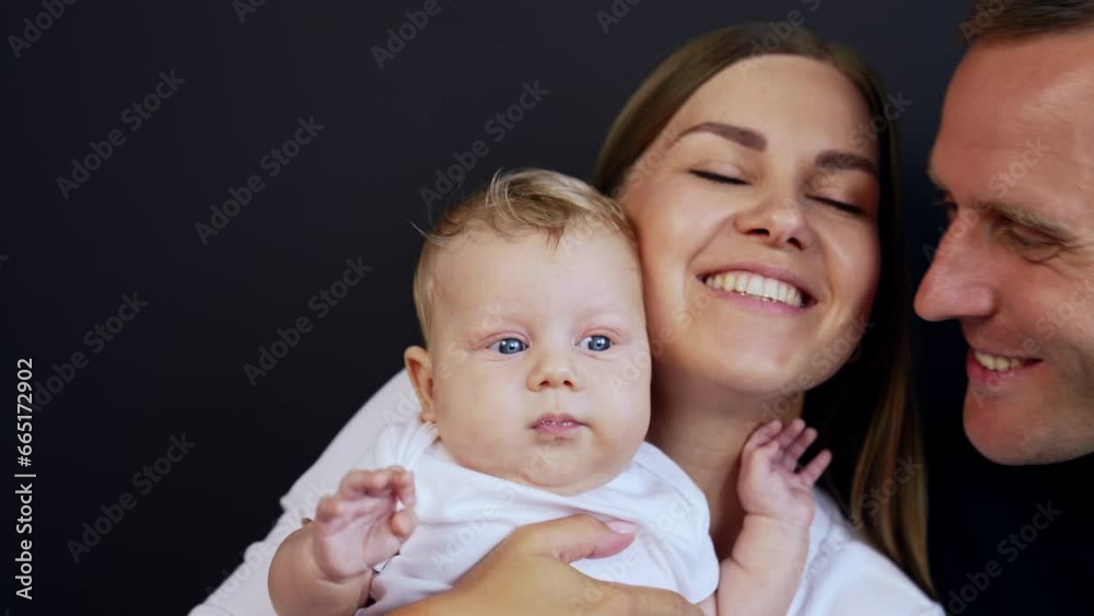Happy smiling mom with her newborn baby. Caucasian man approaches his family. Close up. Black backdrop. Happy smiling mom with her newborn baby. Caucasian man approaches his family. Close up. Black backdrop.
