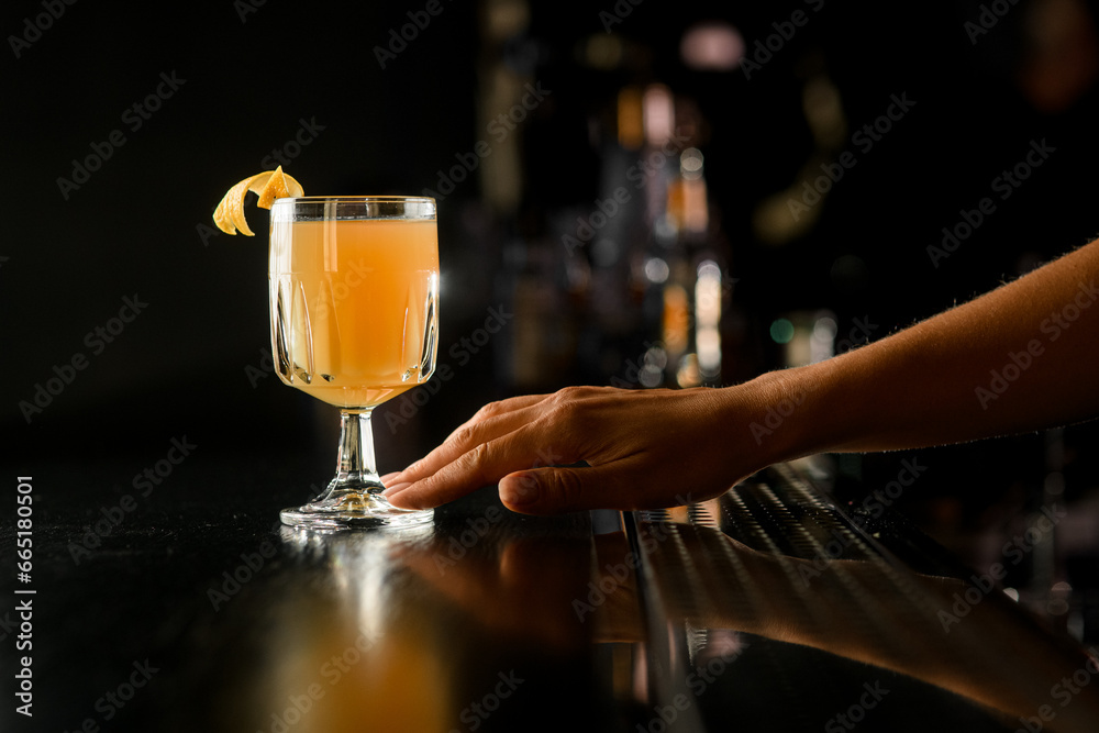 Woman bartender's hand holding refreshing cocktail in old fashioned drinking glass with citrus zest