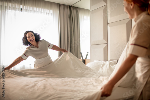 Pair of hotel maids changing the sheets of a bed photo