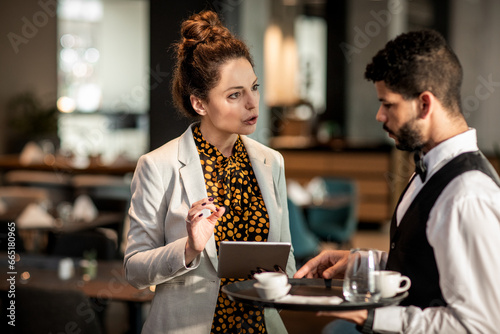 Middle aged businesswoman placing a order with a waiter in a hotel cafe photo