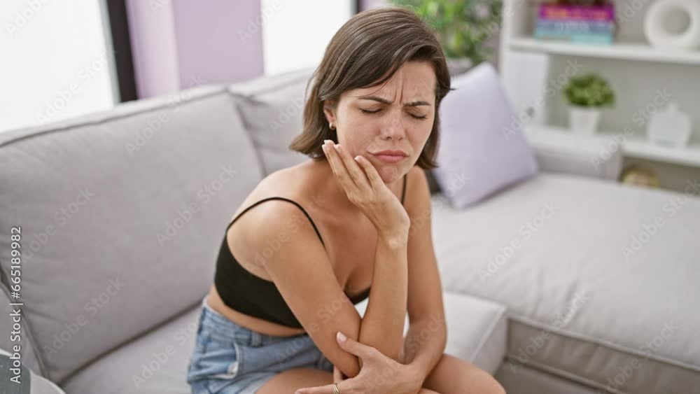 Young beautiful hispanic woman sitting on sofa suffering for toothache at home Young beautiful hispanic woman sitting on sofa suffering for toothache at home