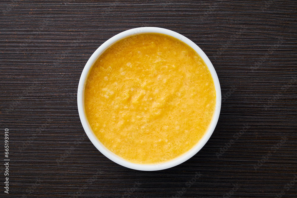 A bowl of pumpkin porridge on a textured dark brown table - an appetizing blend of Thanksgiving and healthy dining, embodying the essence of nourishing traditions. Top view. A bowl of pumpkin porridge on a textured dark brown table - an appetizing blend of Thanksgiving and healthy dining, embodying the essence of nourishing traditions. Top view.