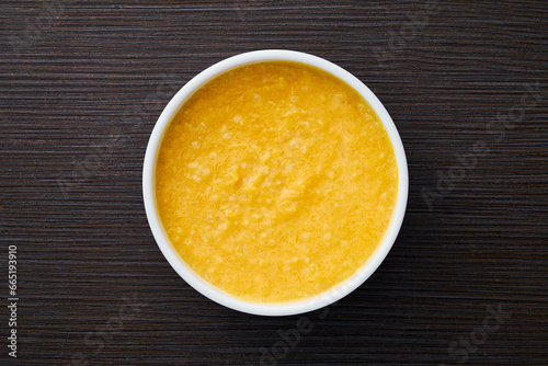 A bowl of pumpkin porridge on a textured dark brown table - an appetizing blend of Thanksgiving and healthy dining, embodying the essence of nourishing traditions. Top view.