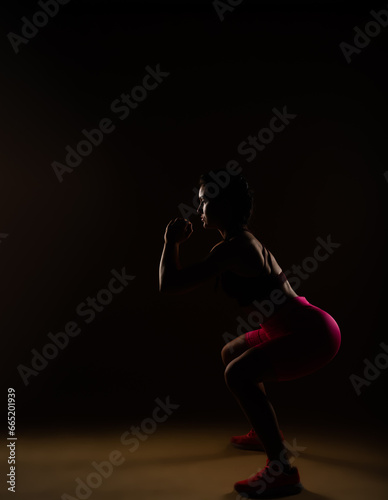 Fit female person doing squats in studio. She is exercising her legs © qunica.com