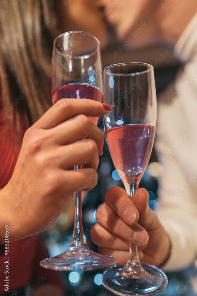 Hands of a man and a woman who kiss while toasting with their crystal glasses in front of the Christmas tree.