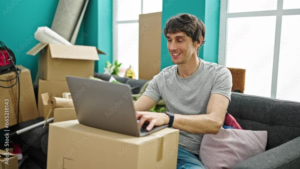Young hispanic man using laptop smiling at new home Young hispanic man using laptop smiling at new home