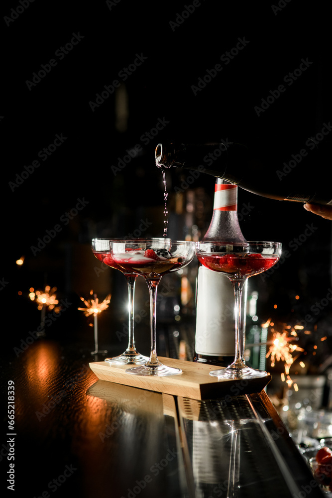 Process of making cocktail: three martini glasses with berries and syrup at the bottom filled with sparkling champagne