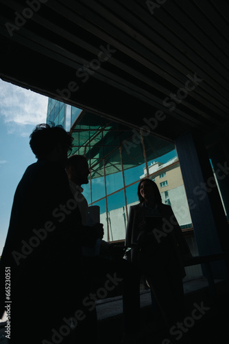 Silhouette of three coworkers having random conversation and smiling after work, before going home