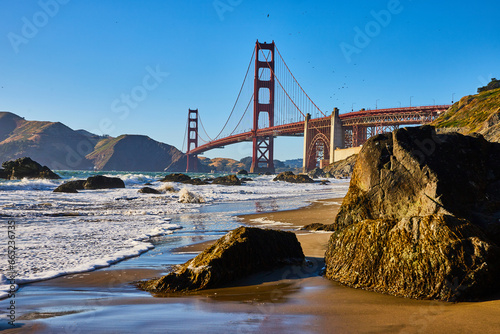 Massive boulders on sandy beach with waves and distant Golden Gate Bridge