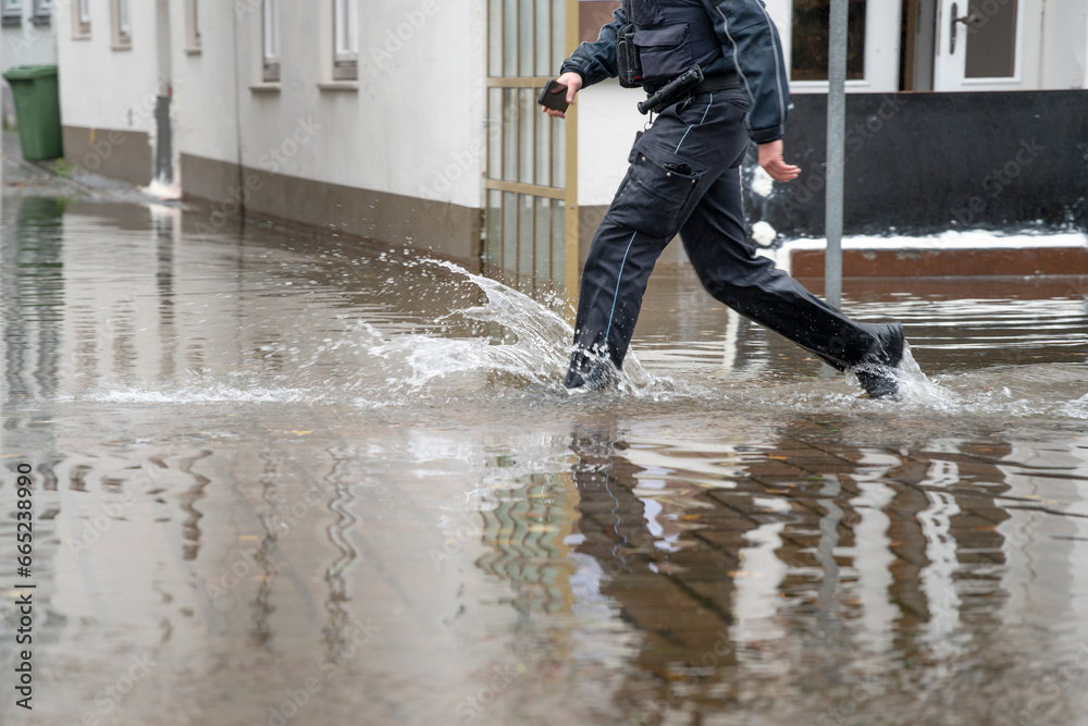 Policeman running through the water of a flooded street during high water of the river Trave in the old town of Lubeck at the Baltic sea in Germany, copy space - obrazy, fototapety, plakaty 