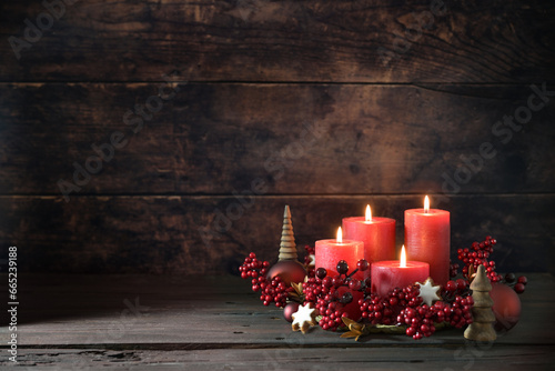 Fourth advent with lighted red candles in a wreath of decoration berries, Christmas balls and cinnamon star cookies against a dark rustic background, copy space, selected focus