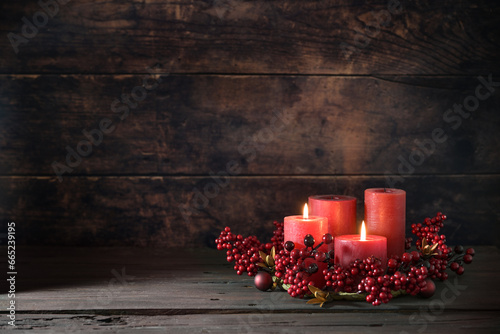 Second Advent with two lit red candles in a wreath from berries with Christmas decoration against a dark rustic wooden background, copy space, selected focus