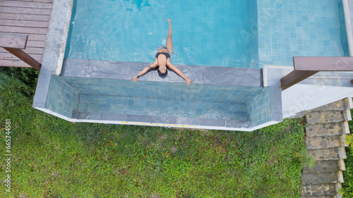 Aerial view of a woman at the edge of a swimming pool enjoying a trip.