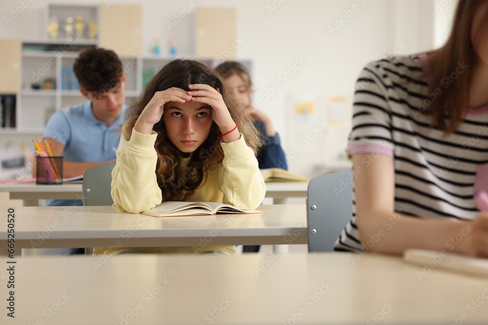 Teen problems. Lonely girl sitting separately from other students in classroom Teen problems. Lonely girl sitting separately from other students in classroom