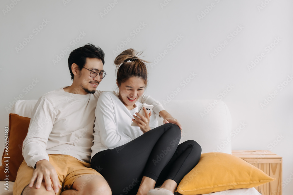 Happy lovely asian couple sharing smartphone to watch together in living room. Happy lovely asian couple sharing smartphone to watch together in living room.