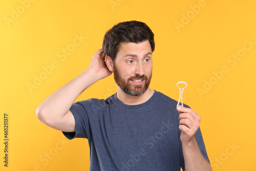 Confused man with tongue cleaner on yellow background