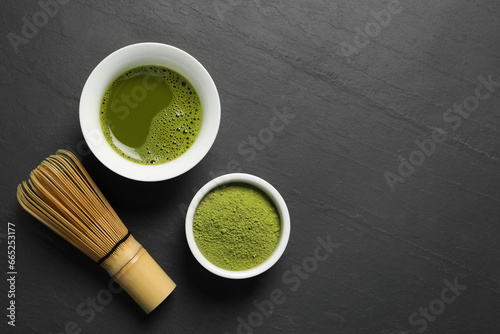 Cup of fresh matcha tea, green powder and bamboo whisk on black table, flat lay. Space for text