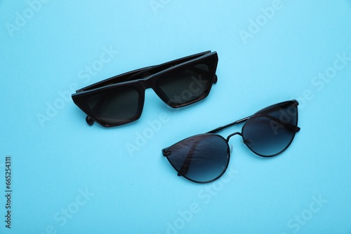 Stylish sunglasses on light blue background, flat lay