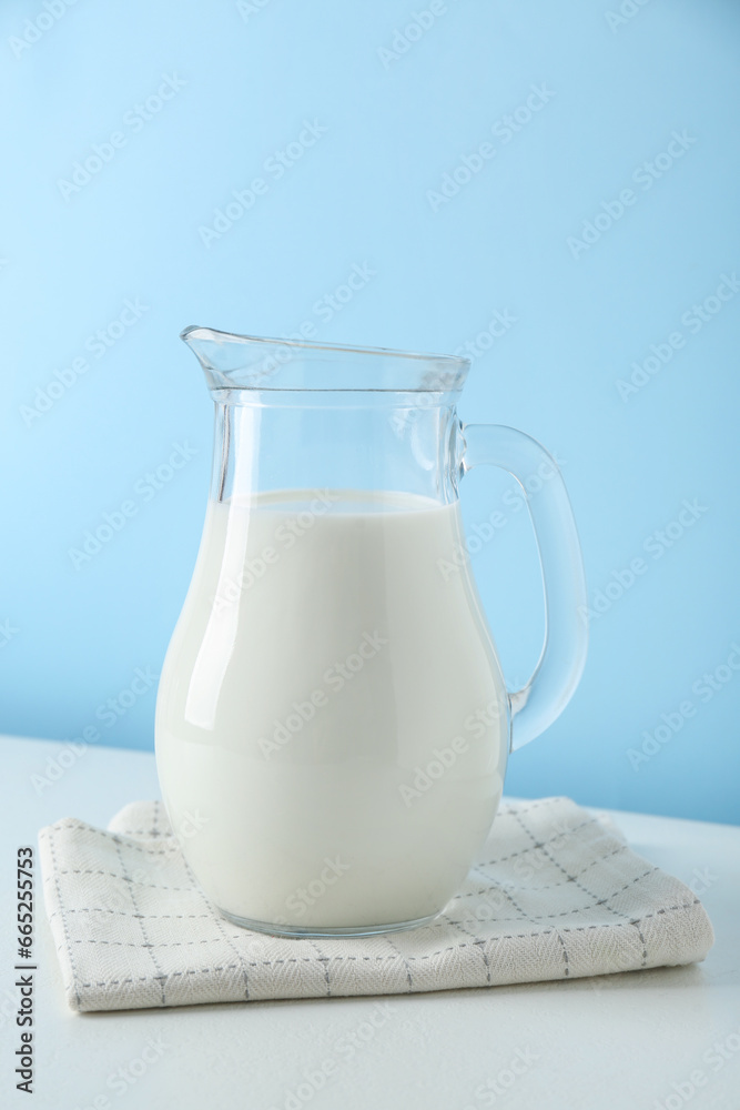 One jug of fresh milk on white table against light blue background One jug of fresh milk on white table against light blue background