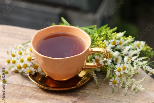 Cup of delicious chamomile tea and fresh flowers outdoors on sunny day  closeup