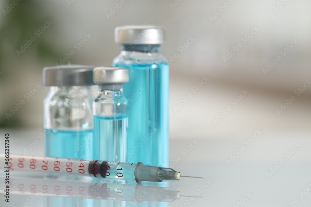 Glass vials with light blue medication and syringe on white table, closeup. Space for text Glass vials with light blue medication and syringe on white table, closeup. Space for text