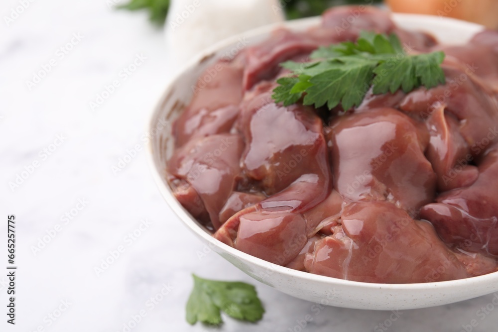 Bowl of raw chicken liver with parsley on white table, closeup. Space for text