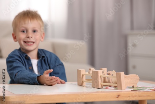 Cute little boy playing with set of wooden animals and fence at table indoors, selective focus with space for text. Child's toy
