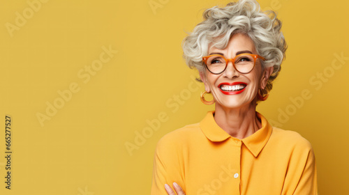 Closeup face of senior business woman standing against yellow background with copy space. Portrait of successful woman in blue shirt feeling confident and looking at camera. Happy mature woman face