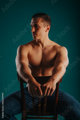 Принти на полотні Strong, muscular man looking aside while posing sitting on a chair in studio