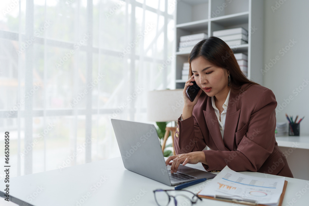 Asian businesswoman, entrepreneur using smartphone and laptop computer to communicate financial business information. Online marketing at the office startup business idea. Asian businesswoman, entrepreneur using smartphone and laptop computer to communicate financial business information. Online marketing at the office startup business idea.