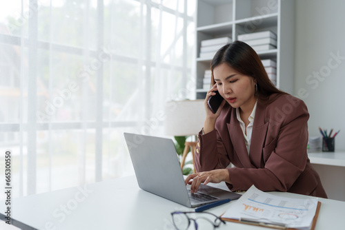 Asian businesswoman, entrepreneur using smartphone and laptop computer to communicate financial business information. Online marketing at the office startup business idea.