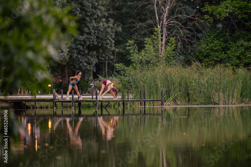 Fit Girls Exercising Together in Green Park with Bridge