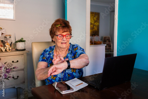 Senior woman at table with laptop using smartwatch wearable technology device photo