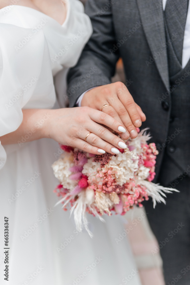 The hands of the bride and groom with rings on the background of a wedding bouquet of white-pink flowers and dried flowers The hands of the bride and groom with rings on the background of a wedding bouquet of white-pink flowers and dried flowers