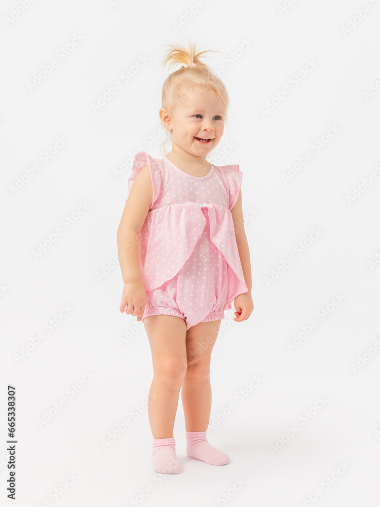 A happy 2-year-old toddler girl in a pink dress laughs on a white background. It stands sideways. A happy 2-year-old toddler girl in a pink dress laughs on a white background. It stands sideways.