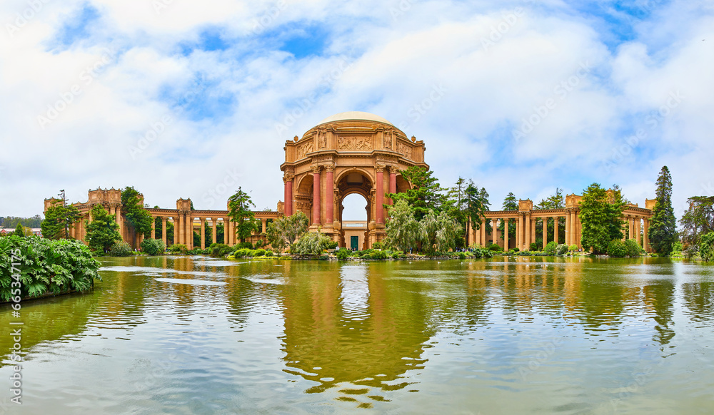 Panorama from across lake water with Palace of Fine Arts under cloudy blue sky