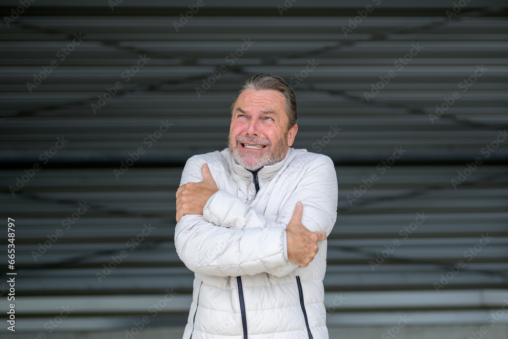 Fototapeta premium Man with a white winter jacket looking shivering at the sky