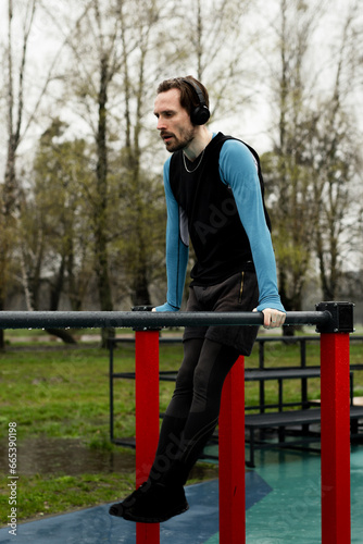 Concept of morning training motivation on fresh air outdoors. Sportsman doing pulling up horizontal bars at court park. Athlete pumping abs body plasticity using metal construction. Gymnastics