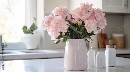 A white vase full of pink flowers is sitting on counter.