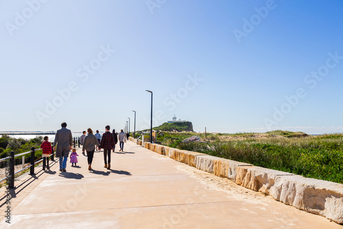 Family walking down Macquarie Pier, Newcastle on sunlit winter day with lighthouse in background photo