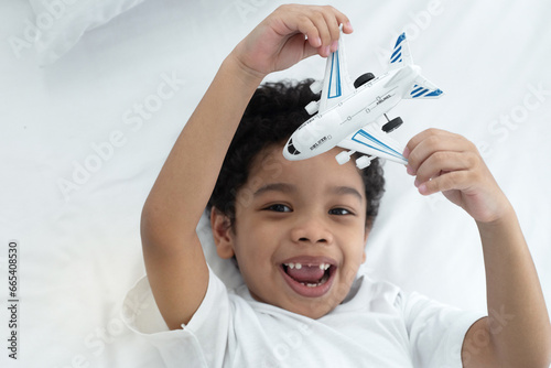 Φωτογραφία Little boy is lying on his bed playing with a toy airplane, pretending the plane