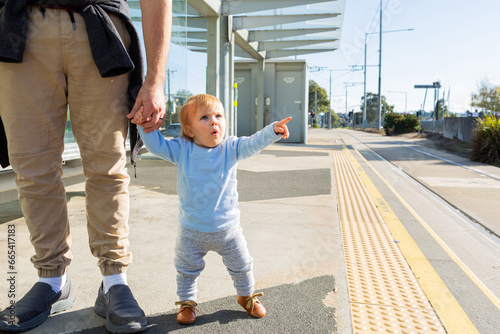 Young toddler pointing at tram station platform holding parents hand photo