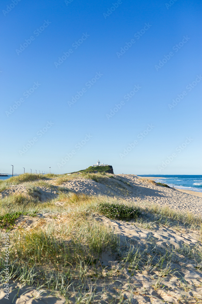 Dunes covered in sea grass with distant headland and lighthouse in Newcastle Dunes covered in sea grass with distant headland and lighthouse in Newcastle