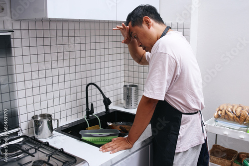 Canvas Print Man hopelessly looking at pile of dirty dishes in kitchen