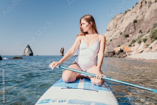 Woman sea sup. Close up portrait of happy young caucasian woman with long hair looking at camera and smiling. Cute woman portrait in a white bikini posing on sup board in the sea © panophotograph