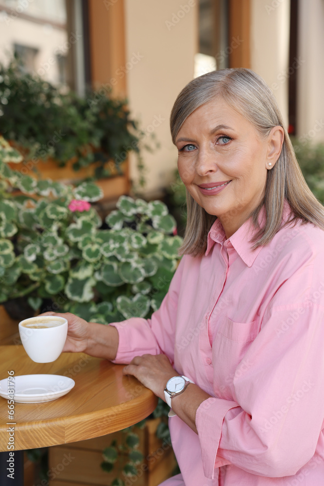 Portrait of beautiful senior woman drinking coffee at table in outdoor cafe