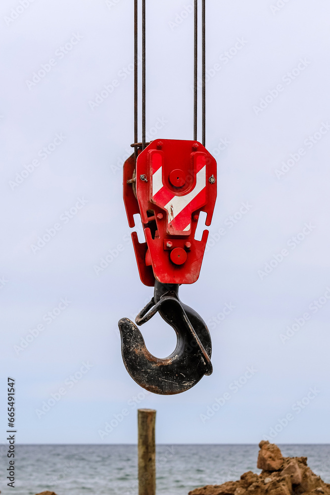 An old lifting hook attached to sheave suspended by wire rope from boom of crane. Construction work on the seashore An old lifting hook attached to sheave suspended by wire rope from boom of crane. Construction work on the seashore