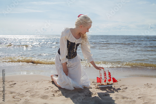 Portrait of perfect young blonde woman with red sail boat on sea beach photo