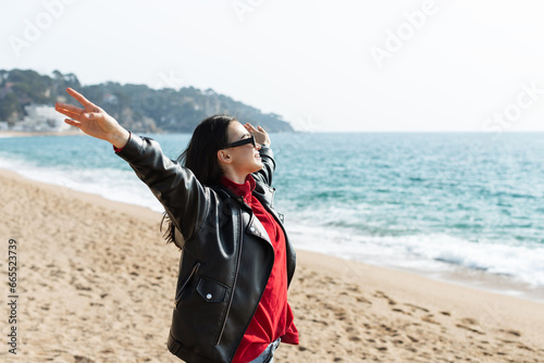 A serene winter beach scene capturing the essence of feminine beauty, freedom, and a refreshing outdoor walk during the sunny day..Young happy woman with raised arms enjoying her vacation in Spain.